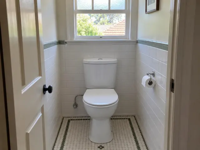 Clean white toilet in a tiled small bathroom with window and doorway in Wahroonga
